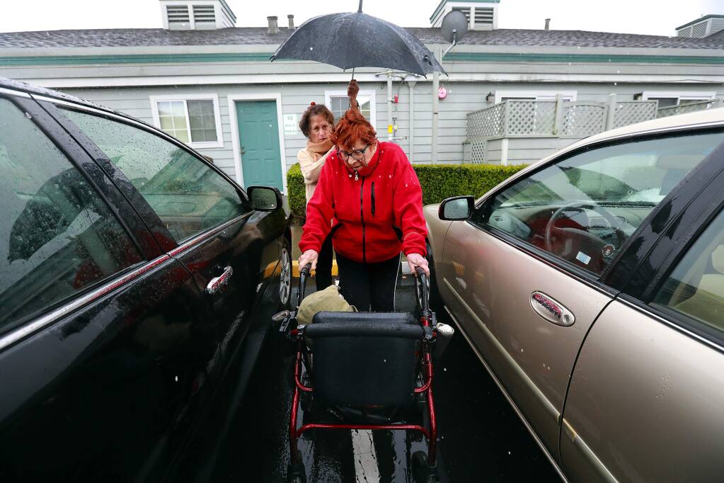 Volunteer Ginger Inglis holds an umbrella for Eleanor Jaquish, 84, as she picks her up from her Petaluma home to take her to her swim exercise class on Friday, February 17, 2017. (John Burgess/The Press Democrat)