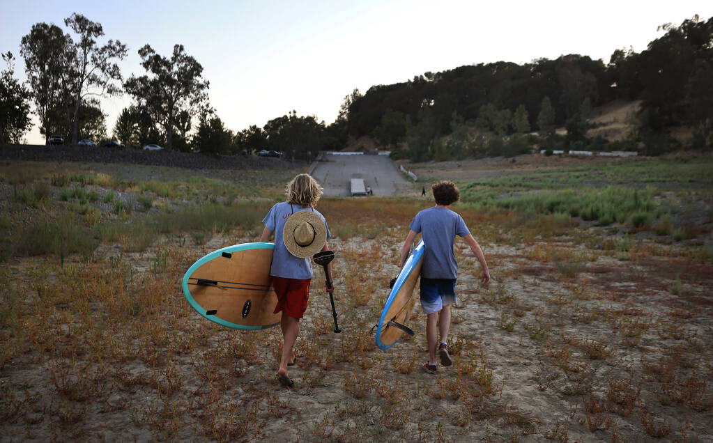 After a late afternoon of paddle boarding, Ukiah residents Zach Kmeall, 17, and Jacob Mello, 18, walk 250 yards from the shoreline (on the dredged boat ramp) to their vehicles, Thursday, July 15, 2021 at Lake Mendocino east of Ukiah.    (Kent Porter / The Press Democrat)