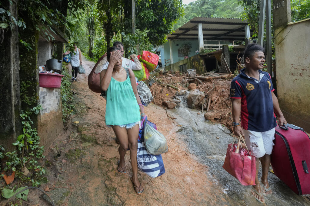 Residents leave their homes after flooding triggered deadly landslides near Juquehy beach in Sao Sebastiao, Brazil, Monday, Feb. 20, 2023. (AP Photo/Andre Penner)