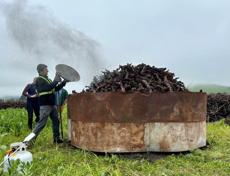 Napachar founder Eric Mayer tosses a biochar pyrolysis display onto a heaping pile of wood waste at Gloria Ferrer Caves and Vineyards Tuesday morning. (Chase Hunter/Index-Tribune)