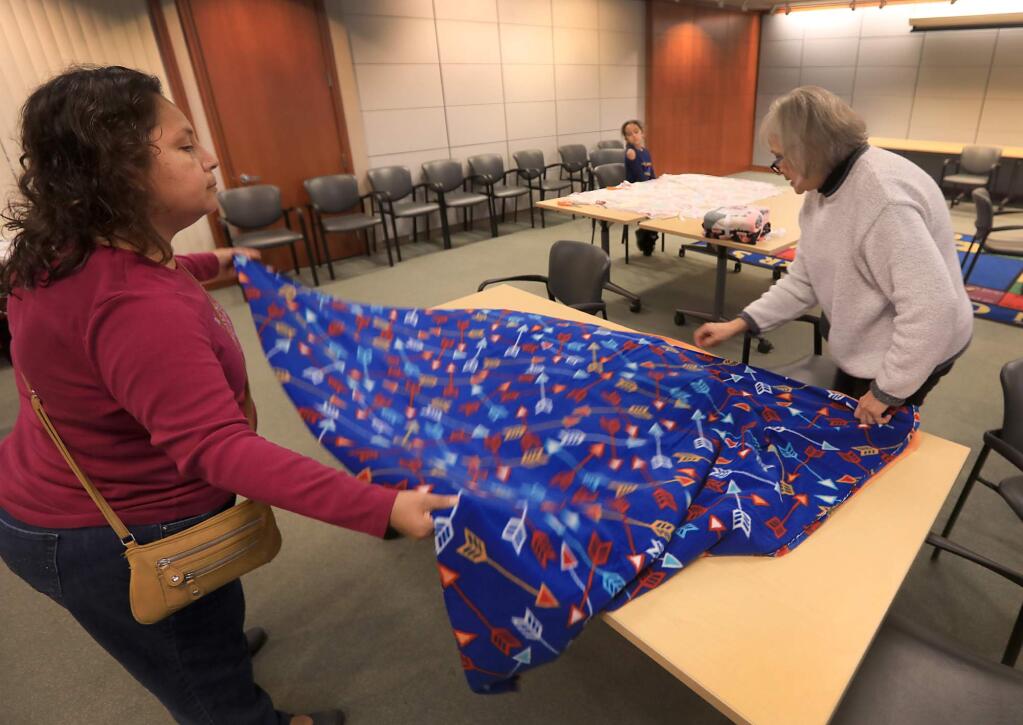 Volunteer Elsa Vera, left and Lisa Sigler, a library associate with the Sonoma County Regional Library in Windsor, prepare to make a quilt out of two blankets as part of the Linus Project a non-profit to help children in need. (Kent Porter / The Press Democrat) 2018