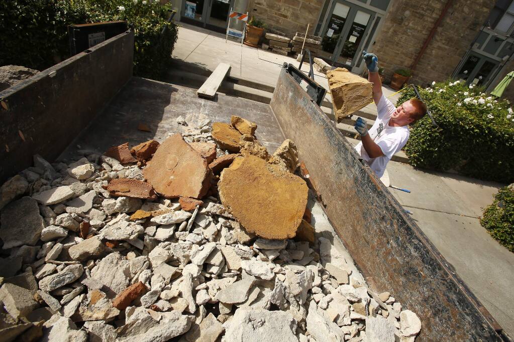 Jake Korpela empties debris caused from last month's earthquake that came off the roof of the Wine Country Real Estate offices along Main Street in Napa on Thursday, September 25, 2014. The building suffered damage from last month's earthquake, but the retrofitting helped keep the building safe. (Conner Jay/The Press Democrat)