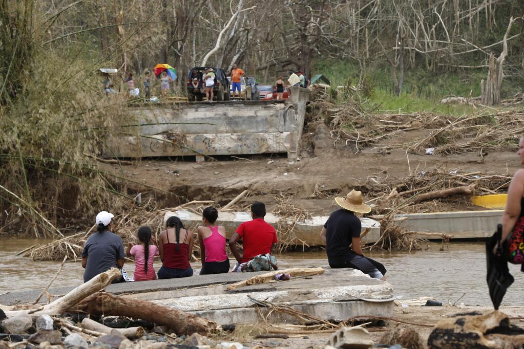 People sit on both sides of a destroyed bridge that crossed over the San Lorenzo de Morovis river, in the aftermath of Hurricane Maria, in Morovis, Puerto Rico, Wednesday, Sept. 27, 2017. A week since the passing of Maria many are still waiting for help from anyone from the federal or Puerto Rican government. But the scope of the devastation is so broad, and the relief effort so concentrated in San Juan, that many people from outside the capital say they have received little to no help. (AP Photo/Gerald Herbert)