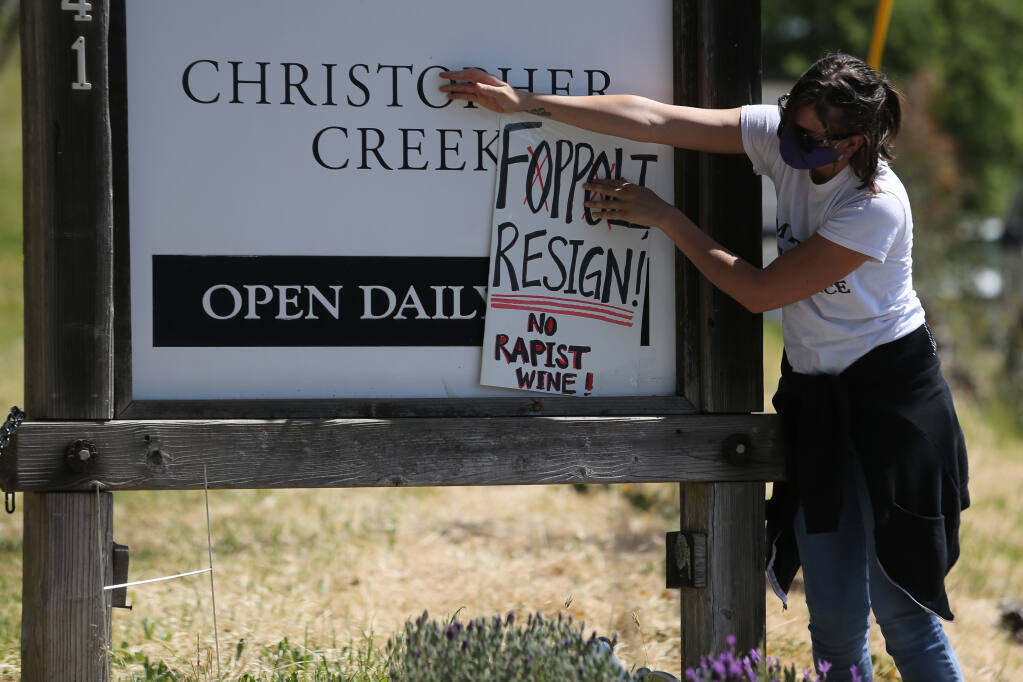 Hollie Clausen tapes up a sign calling for Windsor Mayor Dominic Foppoli to resign during a protest at his family's winery, Christopher Creek Winery near Healdsburg, on Sunday, April 11, 2021. (Beth Schlanker/ The Press Democrat)