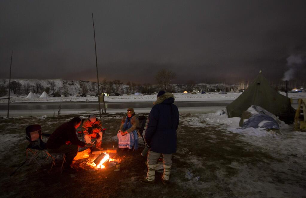 In this Thursday, Dec. 1, 2016 photo, campers sit around a fire along the Cannonball river at the Oceti Sakowin camp where people have gathered to protest the Dakota Access pipeline in Cannon Ball, N.D. So far, those fighting the Dakota Access pipeline have shrugged off the heavy snow, icy winds and frigid temperatures that have swirled around their encampment on the North Dakota grasslands. But if they defy next week's government deadline to abandon the camp, demonstrators know the real deep freeze lies ahead. (AP Photo/David Goldman)