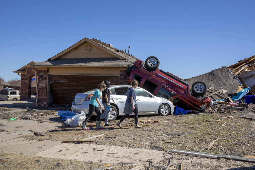 Neighbors walk in front of a home damaged at Wheatland Drive and Conway Drive on Monday, Feb. 27, 2023 in Norman, Okla. The damage came after rare severe storms and tornadoes moved through Oklahoma overnight. (AP Photo/Alonzo Adams)