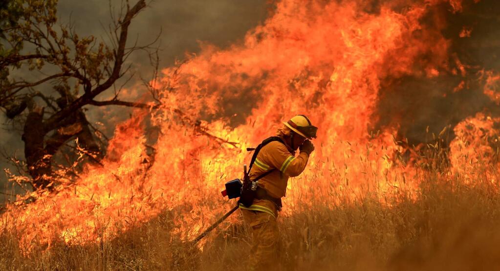 A Geyserville firefighter shields his face as a backfire burns with intensity off Morgan Valley Road on the Rocky Fire, Thursday July 30, 2015 near Lower Lake. (Kent Porter / Press Democrat) 2015
