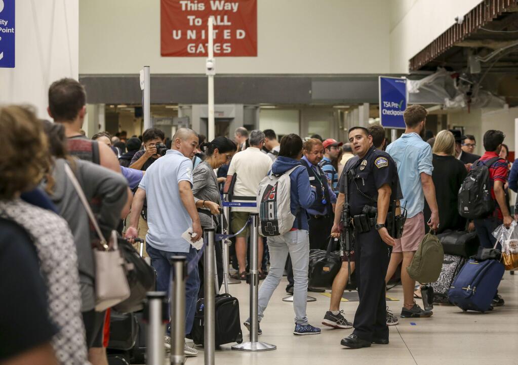 A police officer stands guard as passengers wait in line at Terminal 7 in Los Angeles International Airport, Sunday, Aug. 28, 2016. Reports of a gunman opening fire that turned out to be false caused panicked evacuations at Los Angeles International Airport on Sunday night, while flights to and from the airport saw major delays. Passengers who fled had to be rescreened through security. A search through terminals brought no evidence of a gunman or shots fired, Los Angeles police spokesman Andy Neiman said. (AP Photo/Ringo H.W. Chiu)