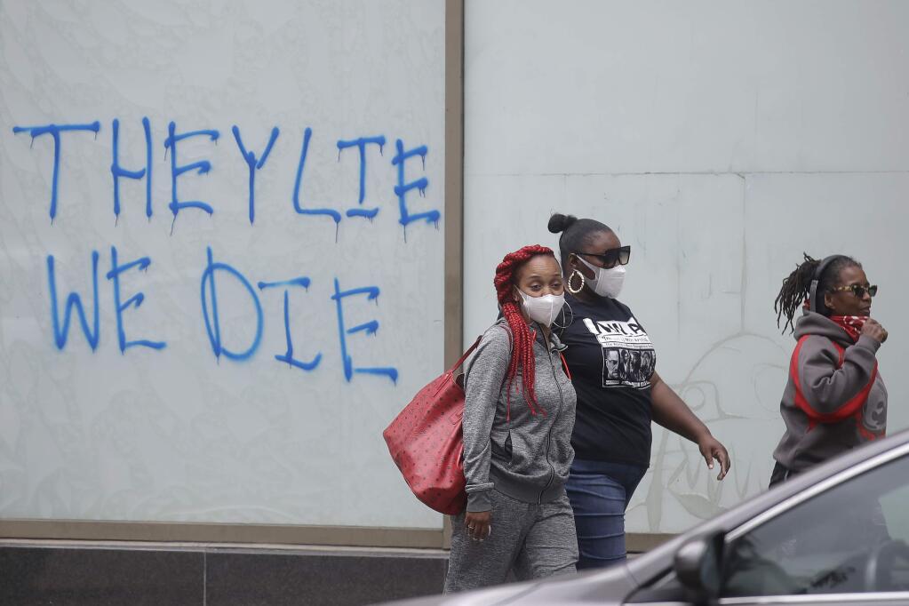Women wear face masks while walking past graffiti on a wall after protests over the death of George Floyd in Oakland, Calif., Saturday, May 30, 2020. Protests across the country have escalated over the death of George Floyd who died after being restrained by Minneapolis police officers on Memorial Day, May 25.(AP Photo/Jeff Chiu)