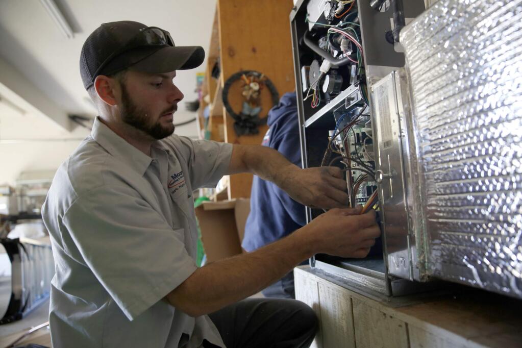 Micah Pierce, a technician with Moore Heating and Air Conditioning, installs a new furnace at a home on Wednesday, December 31, 2014 in Graton, California . (BETH SCHLANKER/ The Press Democrat)