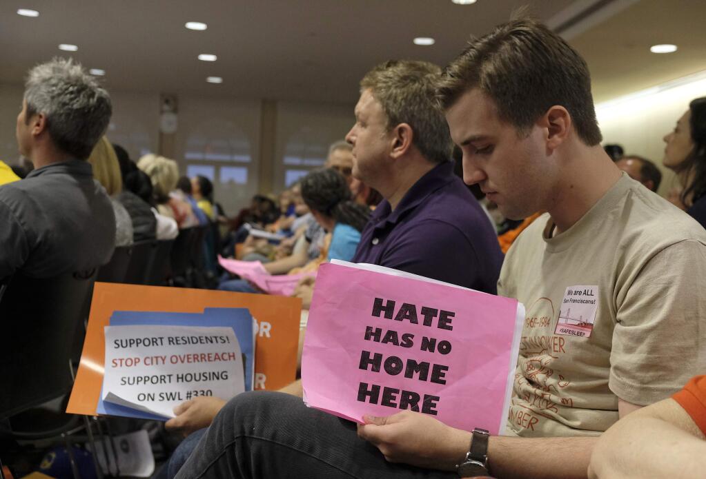 Two men hold signs while listening to public comment about a proposed homeless shelter during a meeting of the Port Commission Tuesday, April 23, 2019, in San Francisco. San Francisco port commissioners are deciding whether to approve a new homeless shelter along the city's touristy and residential Embarcadero.(AP Photo/Eric Risberg)
