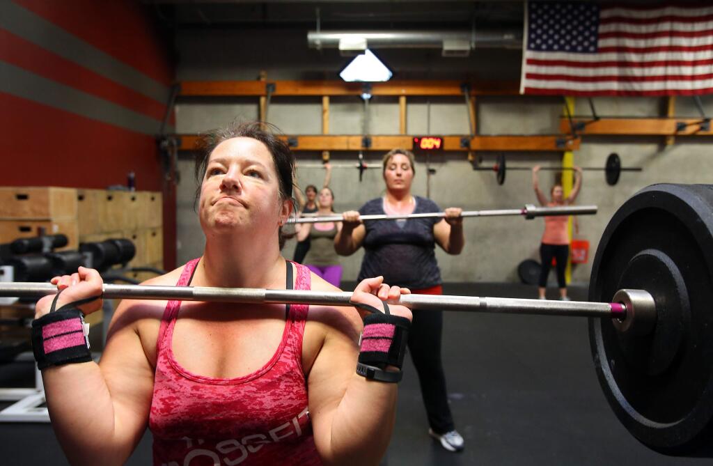 PHOTO: 1 BY CHRISTOPHER CHUNG/ THE PRESS DEMOCRAT -Katie Paulson lifts weights while wearing a Garmin Vivofit activity tracker on her left wrist at Crossfit Force in Santa Rosa. When they burn enough calories each month, Paulson and her husband are able to save money into a health savings account through a health wellness program at her husband's work.