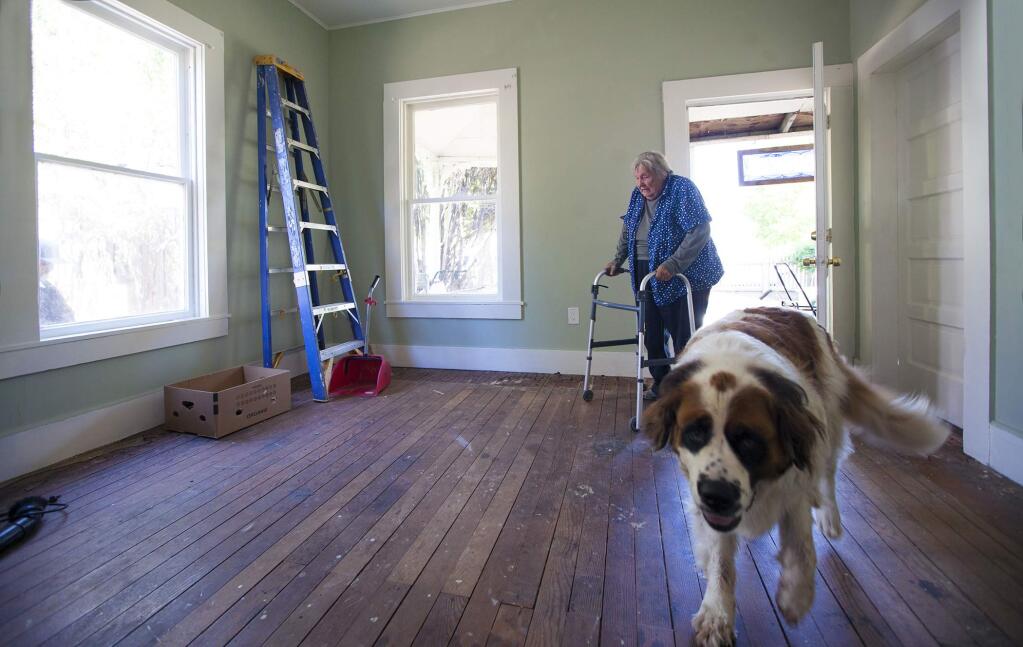 Irma Castillo, ever grateful for the efforts of all those who have volunteered to make her house habitable, and her faithful companion Tobie, step into the newly renovated living room of her 100-year-old Broadway house in Sonoma, which now needs only a new floor to be complete. (Photo by Robbi Pengelly/Index-Tribune)