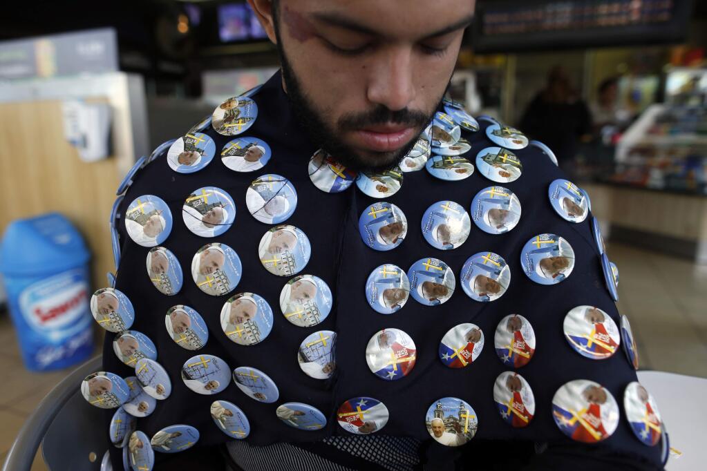 A vendor wears a poncho displaying Pope Francis souvenir pins before the start of a public papal Mass at O'Higgins Park in Santiago, Chile, Tuesday, Jan. 16, 2018. Chileans turned out in droves for the Mass celebrated by Francis, where St. John Paul celebrated Mass three decades ago. (AP Photo/Luis Hidalgo)