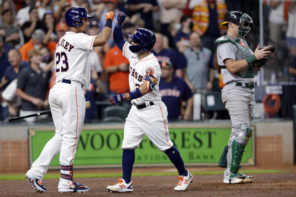 The Houston Astros’ Michael Brantley; left, and Jose Altuve high-five next to Oakland Athletics catcher Sean Murphy, right, after Altuve’s home run during the seventh inning on Thursday, April 8, 2021, in Houston. (Michael Wyke / ASSOCIATED PRESS)