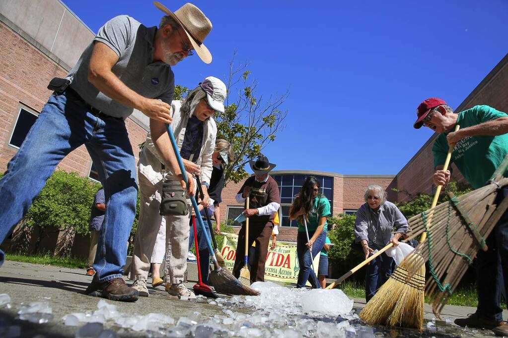 Terry Winter, left, Vicki Smith, Liz Finn, second from right, and Marty Bennett sweep away ice, at the Sonoma County Adult Detention Facility, in a demonstration to protest the Sonoma County Sheriff's Office sharing of information of undocumented inmates with the U.S. Immigration and Customs Enforcement, in Santa Rosa on Monday, May 1, 2017. (Christopher Chung/ The Press Democrat)