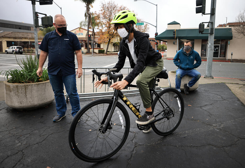 Sunridge Charter School 8th grader Adam Lacey tries out a donated road bike by Trek Bicycle Santa Rosa service manager Phil Heydorn, left. Adam's father Paui Harlin is at right, Wednesday, Dec. 15, 2021.  (Kent Porter / The Press Democrat) 2021