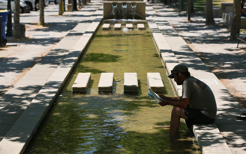 Bill Herrick stays cool by soaking his legs in the fountain while reading a book at the Windsor Town Green on Thursday, June 17, 2021.  (Christopher Chung/ The Press Democrat)
