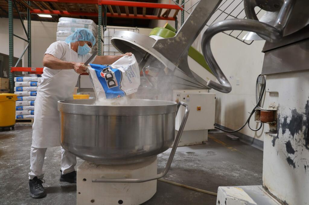Felipe Carrillo pours a bag of flour into large mixing bowl while making sourdough bread at the Costeaux French Bakery production facility in Santa Rosa on Wednesday, April 15, 2020. (Christopher Chung/ The Press Democrat)