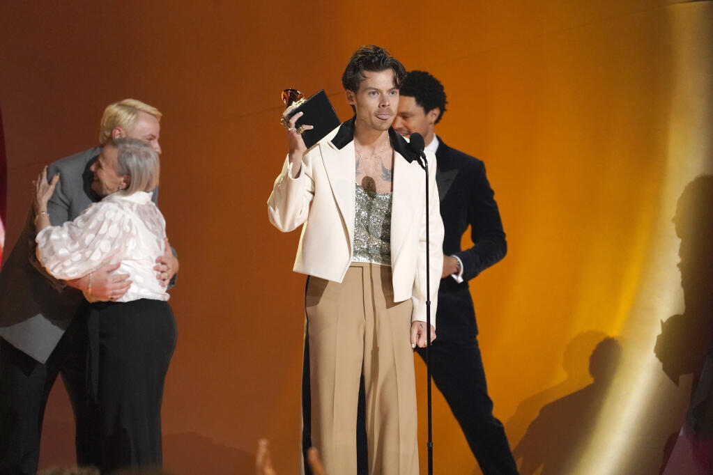 Kid Harpoon, far left embraces fan Reina, while Harry Styles, center, accepts the award for record of the year for "Harry's House" at the 65th annual Grammy Awards on Sunday, Feb. 5, 2023, in Los Angeles. Host Trevor Noah looks on from right.(AP Photo/Chris Pizzello)