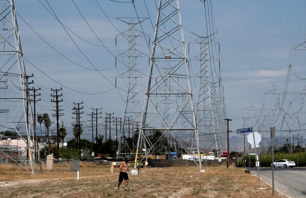 A jogger runs in extreme heat under high tension electrical lines in the North Hollywood section of Los Angeles on Saturday, Aug. 15, 2020. California has ordered rolling power outages for the first time since 2001 as a statewide heat wave strained its electrical system. (AP Photo/Richard Vogel)