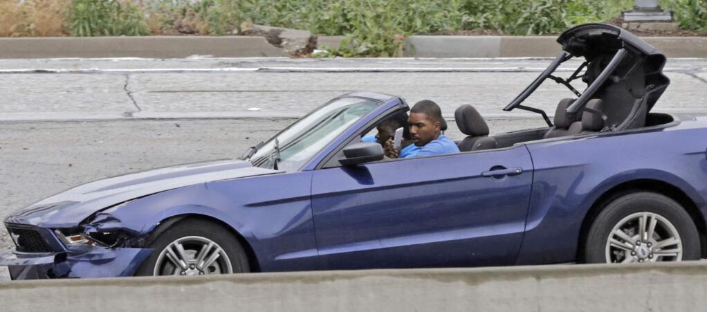 The driver of a convertible blue Mustang holds a personal device and looks into his side-view mirror as he speeds down the busy Harbor Freeway (Interstate 110) in downtown Los Angeles, as he and a passenger are pursued in a chase on rainy Southern California streets and highways, Thursday, April 7, 2016. Authorities arrested the two burglary suspects after they stopped the car in a South Los Angeles neighborhood, exchanged high-fives with onlookers and took selfies before officers arrived several minutes later and handcuffed them. (AP Photo/Reed Saxon)
