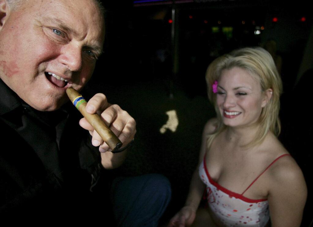 FILE - In this April 7, 2005, file photo, Moonlite Bunny Ranch owner Dennis Hoff smokes a cigar at his brothel's entrance in Mound House, Nev. Hof, a legal pimp who has fashioned himself as a Donald Trump-style Republican candidate has died, Nevada authorities said Tuesday, Oct. 16, 2018. (AP Photo/Brad Horn