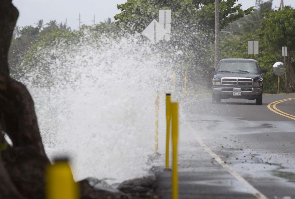 The driver of a pickup truck slows down to avoid being sprayed by waves breaking off of Kamehameha Highway in Honolulu on Friday, Aug. 8, 2014. Due to the effects of Tropical Storm Iselle, surf was stronger than normal on Oahu's windward side. Iselle came ashore onto the Big Island early Friday as a weakened tropical storm, while Hurricane Julio, behind it, is forecasted to pass north of the islands. Iselle is the first tropical storm to hit the state in 22 years. (AP Photo/Eugene Tanner)