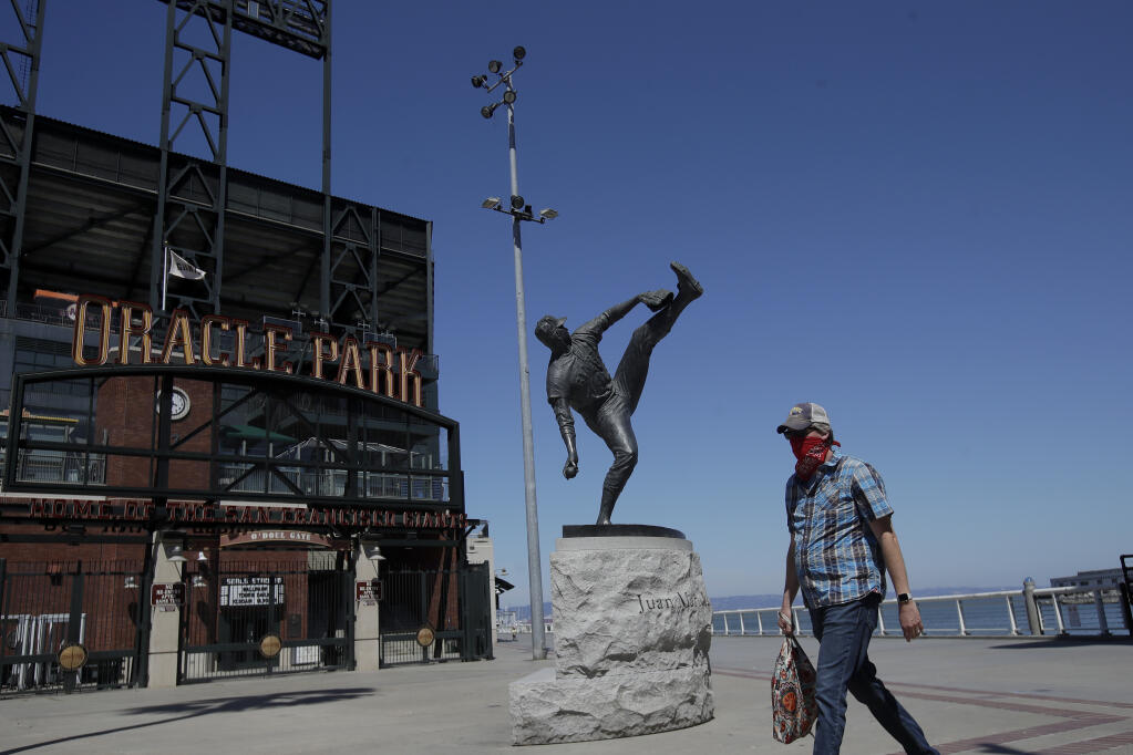 A man wearing a mask walks by the statue of Hall of Fame pitcher Juan Marichal outside of the Giants’ Oracle Park in San Francisco, Thursday, June 25, 2020. (Jeff Chiu / ASSOCIATED PRESS)