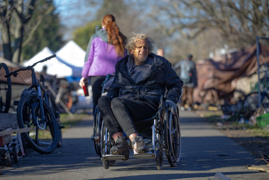 Patrick Donohue, 64, wheels his way off the Joe Rodota Trail after getting help from street outreach worker Cheryl Rood while packing up his camp along Joe Rodota Trail at Roseland Avenue in Santa Rosa, Tuesday, Jan. 24, 2023. (Chad Surmick/The Press Democrat)