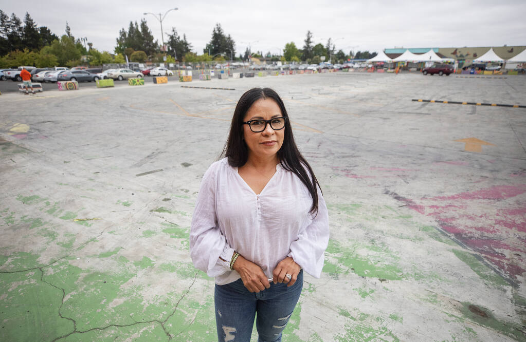 Sylvia Camacho stands in the proposed site of a proposed 175-unit housing development in the middle of the present Roseland Village Shopping Center. Camacho welcomes new customers but fears the development will leave her old customers without a place to park. (John Burgess / The Press Democrat)