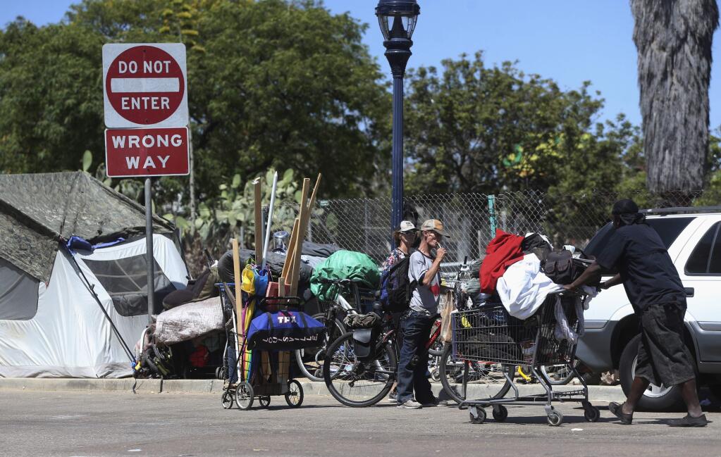 Homeless people crowd a parkway with tents and makeshift housing Wednesday, July 6, 2016, in San Diego. Another San Diego homeless man was seriously injured early Wednesday by an attacker police say struck while he was asleep and tried to set him on fire, the latest in a spate of attacks on transients that have left two dead. (AP Photo/Lenny Ignelzi)