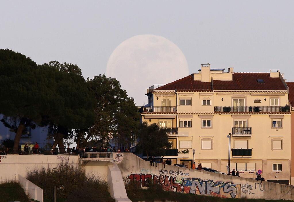 People watch the sunset from the top of a hill as the full moon rises behind them Sunday, Jan. 20 2019, in Lisbon. Sunday night, the Earth will slide directly between the moon and the sun, creating a total lunar eclipse. It will also be the year's first supermoon, when a full moon appears a little bigger and brighter thanks to its slightly closer position. (AP Photo/Armando Franca)