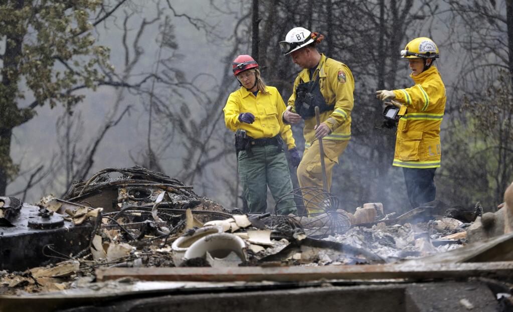 Firefighter Sean Norman, center, and search dog handlers Mary Cablk, left, and Lynne Engelbert look over the remains of a home in the Anderson Springs area of a man missing following a wildfire days earlier Wednesday, Sept. 16, 2015, near Middletown, Calif. Aided by drought, the flames have consumed more than 100 square miles since the fire sped Saturday through rural Lake County, less than 100 miles north of San Francisco. Cooler weather helped crews gain ground and the fire was 30 percent contained Wednesday. (AP Photo/Elaine Thompson)