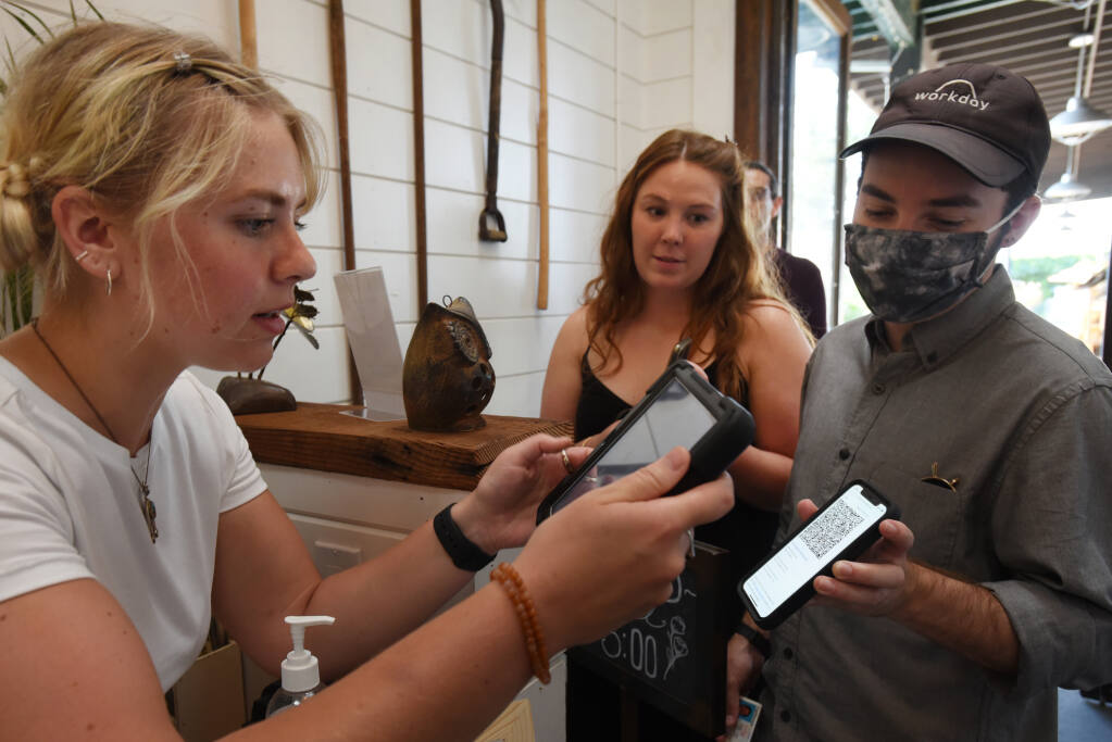 Fern Bar hostess Michaela Codding, left, scans a QR code to verify COVID-19 vaccinations of guests Michael Estems, 26, right, and Katie-Lauren Dunbar, 26, both from Santa Rosa, on Wednesday, July 28, 2021, in Sebastopol. (Erik Castro / For The Press Democrat)
