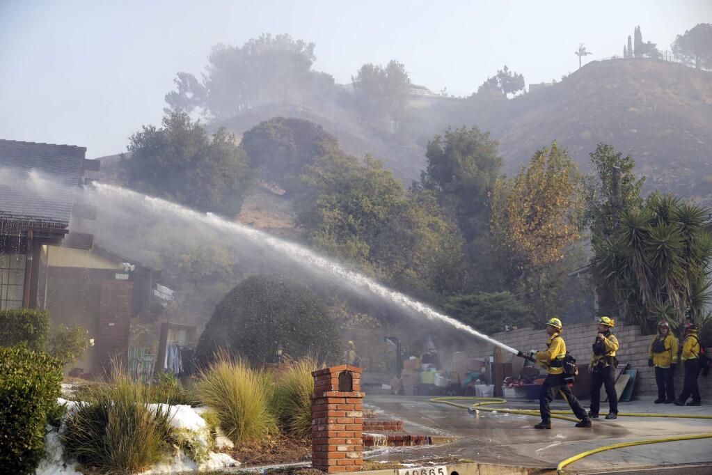 Firefighters hose down the roof of a house damaged by a wildfire Friday, Oct. 11, 2019, in Porter Ranch, Calif. (AP Photo/Marcio Jose Sanchez)