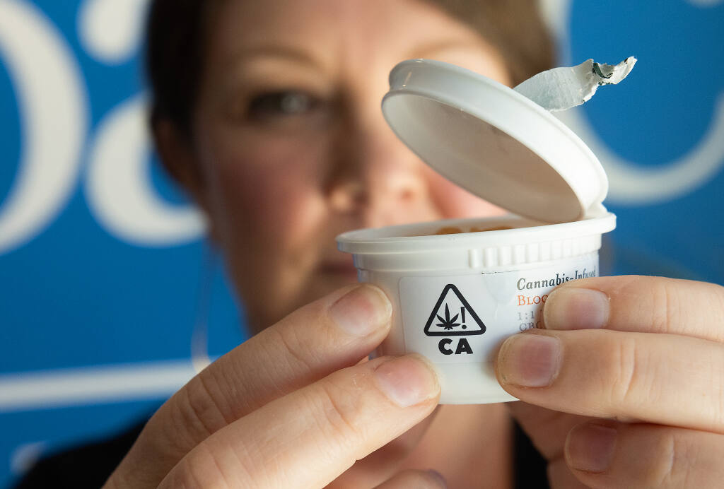 Tess Kofoid, vice president of marketing and sales at SPARC cannabis dispensary in Santa Rosa shows the double child-resistant packaging, one a tough to peel sealing tape and then a difficult squeeze from the sides at a designated point, required to open a container of Wyld cannabis-infused gummies, Friday, April 28, 2023. (John Burgess / The Press Democrat)
