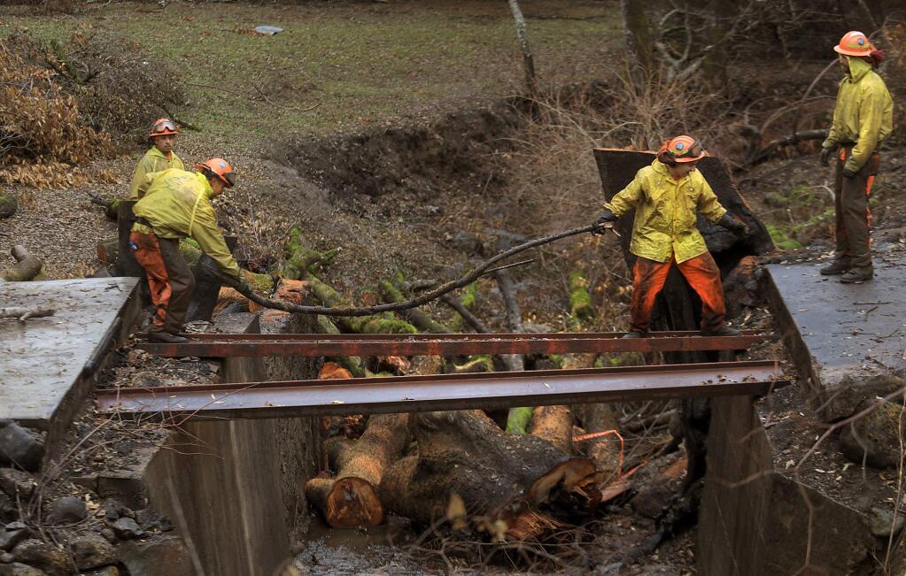 A Konocti Cal Fire inmate crew use steel girders to cross a burned out bridge on Riebli Road, Wednesday Nov. 15, 2017 as they remove debris from creek in front of a burned home. Numerous wood bridges were burned in the October fires, preventing crews from cleaning home sites that were destroyed. (Kent Porter / Press Democrat) 2017