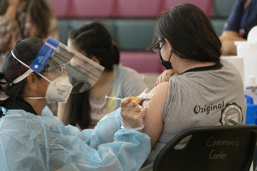 FILE - In this May 27, 2021, file photo, sisters Guadalupe Flores, 15, right, and Estela Flores, 13, left, from East Los Angeles, get vaccinated with the Pfizer's COVID-19 vaccine by licensed vocational nurse Rita Orozco, far left, at the Esteban E. Torres High School in Los Angeles.  (AP Photo/Damian Dovarganes, File)