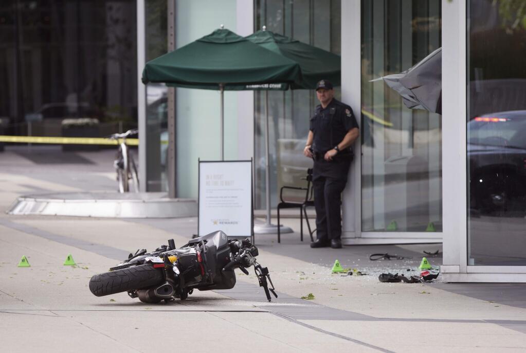 A police officer stands at the scene as a motorcycle lies on the ground after a female stunt driver working on the movie 'Deadpool 2' died after a crash on set, in Vancouver, B.C., on Monday Aug. 14, 2017. Vancouver police say the driver was on a motorcycle when the crash occurred on the movie set on Monday morning. (Darryl Dyck/The Canadian Press via AP)