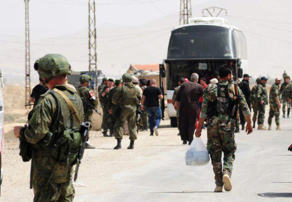 This photo released by the Syrian official news agency SANA, shows Russian soldiers and Syrian government forces gathering next to a bus during the evacuation of rebel fighters from the Army of Islam and their families from the town of Dumayr, northeast of Damascus, Syria, Thursday, April 19, 2018. Syrian state media said Thursday that hundreds of rebel fighters in Dumayr, have handed in their weapons and started to leave the area under an evacuation deal moving them to opposition-held areas in the north, effectively surrendering their turf to government forces. (SANA via AP)