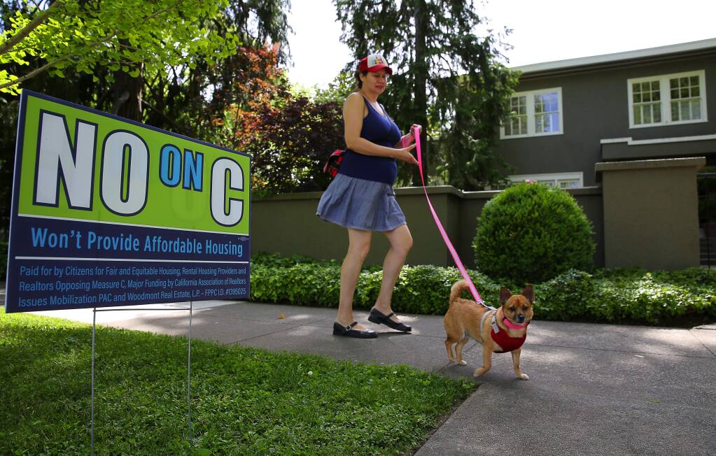 A supporter of Measure C, who did not want her name used, walks past a sign opposed to Measure C along McDonald Avenue, in Santa Rosa on Friday, May 5, 2017. (Christopher Chung/ The Press Democrat)