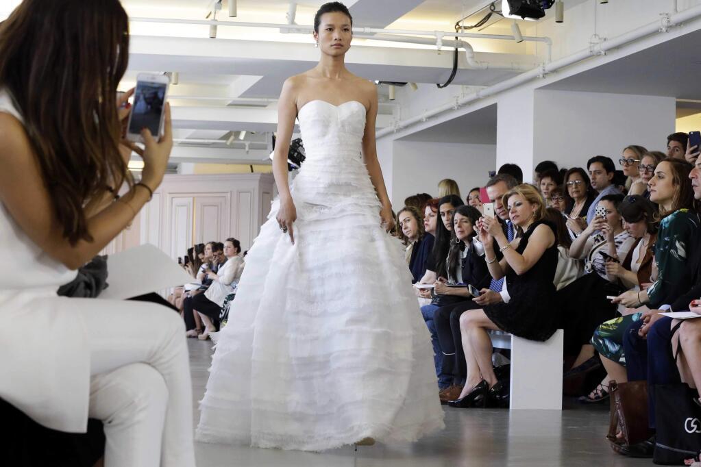 In this April 18, 2015 photo, a model wears a creation from the Oscar de la Renta Bridal Spring 2016 collection in New York. Peter Copping, hired last October as artistic director of the luxury label, retained much of the classic de la Renta glamour but added a few more modern-looking silhouettes, some new takes on fabric work, and some silvery sequins. (AP Photo/Mary Altaffer)