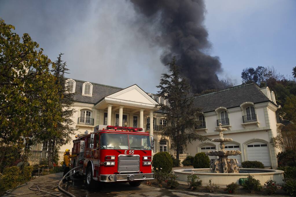 A fire truck is parked outside a mansion as smoke from a wildfire rises behind the property Wednesday, Dec. 6, 2017, in the Bel-Air neighborhood of Los Angeles. (AP Photo/Jae C. Hong)