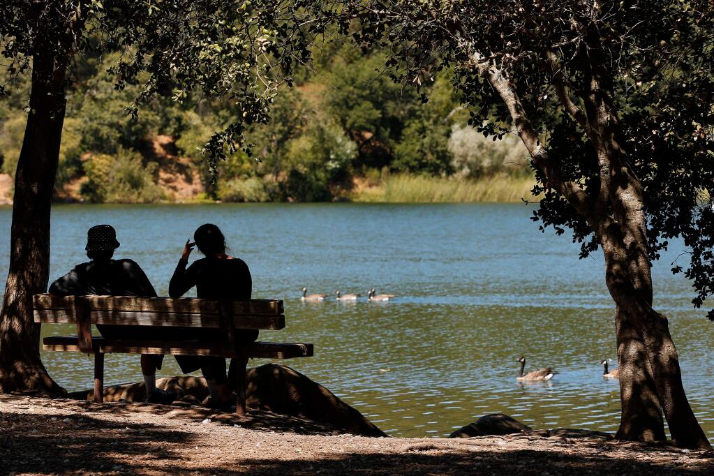 A couple stays cool in the shade while they chat beside Lake Ralphine in Santa Rosa, California, on Wednesday, August 14, 2019. (Alvin Jornada / The Press Democrat)