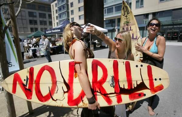 Adrienne Moore of San Francisco uses chocolate syrup in place of oil to prove a point on surfers Kathleen Egan, left and Emilia Lipcsei, during a protest rally, Thursday April 16, 2009 outside of a hearing on offshore energy development, at the UC San Francisco Mission Bay Campus.(Kent Porter / The Press Democrat)2009