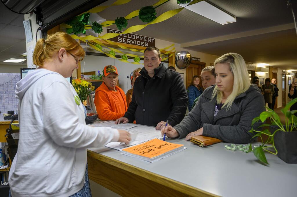 In this photo taken Thursday, March 28, 2019, Anne Vierra,with the town of Paradise, takes payment for the first building permit since the Camp Fire as Jason and Meagann Buzzard plan to rebuild their home in Paradise, Calif. Small signs of rebuilding a Northern California town destroyed by wildfire are sprouting this spring, including the issuing of the first permit to rebuild one of the 11,000 homes destroyed in Paradise five months ago. A city hall clerk on Thursday issued the couple a building permit to replace their home destroyed by the Nov. 8 fire that killed 85 people. The couple told reporters they never thought about leaving. Paradise Mayor Jody Jones said the Buzzards' permit is a sign that the town will rebuild.(Hector Amezcua/The Sacramento Bee via AP)