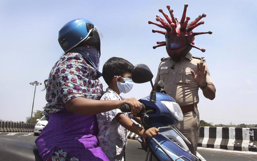FILE-In this March 28, 2020 file photo, police officer Rajesh Babu wears a helmet representing the coronavirus, and requests commuters to stay home during countrywide lockdown in Chennai, India. Health officials are rushing to contain a coronavirus outbreak in one of Asia's largest fruit and vegetable markets in this southern Indian city. (AP Photo/R. Parthibhan, File)