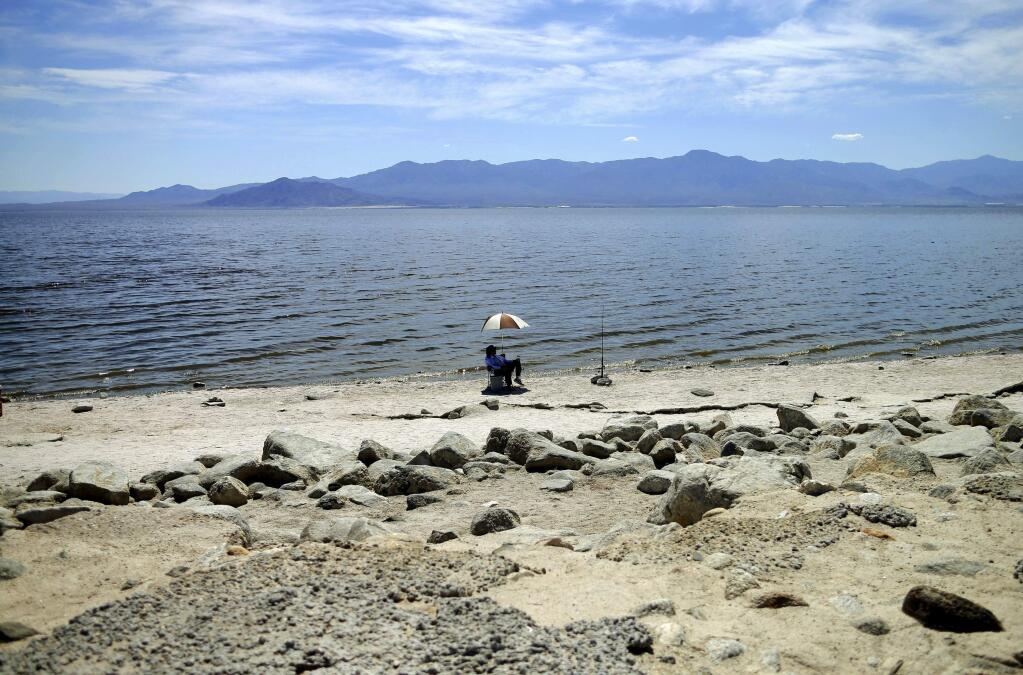 FILE - In this April 30, 2015 file photo, a man fishes along the receding banks of the Salton Sea near Bombay Beach, Calif. An odor advisory has been issued for the Coachella Valley area of Southern California because of naturally occurring processes in the Salton Sea that produce a gas with a rotten egg smell. The South Coast Air Quality Management District issued the advisory Sunday, Aug. 18, 2019, due to elevated levels of hydrogen sulfide detected immediately downwind of the huge desert lake. (AP Photo/Gregory Bull, File)