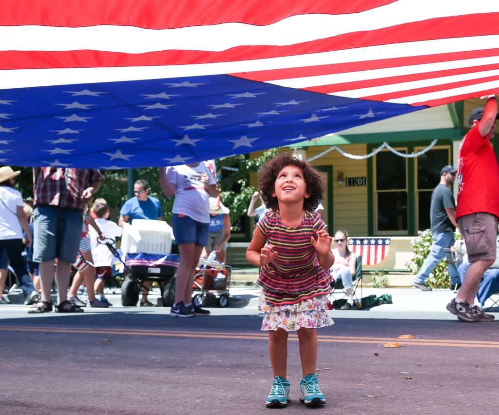 Emma Guevara, 4, of Rohnert Park plays under the flag at the end of the 39th annual Penngrove Parade on Sunday, July 6, 2014.